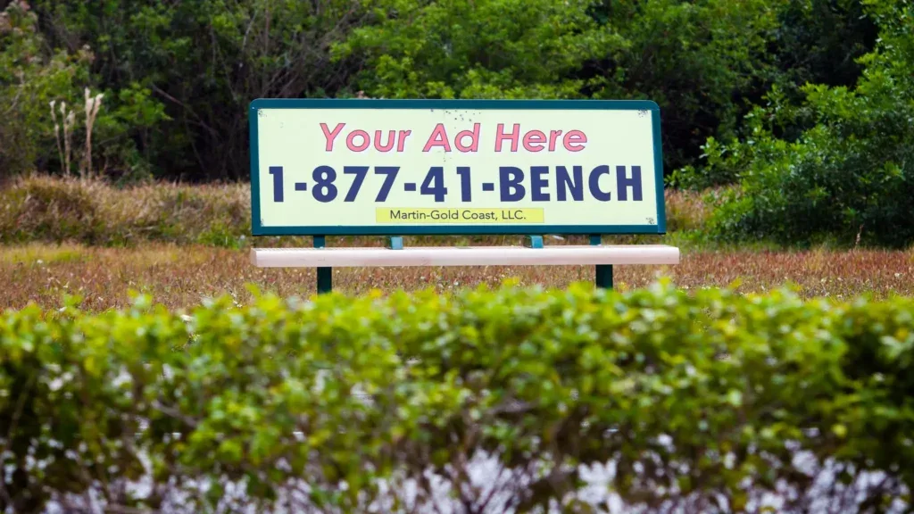A public bench with a "your ad here" sign and a contact number.