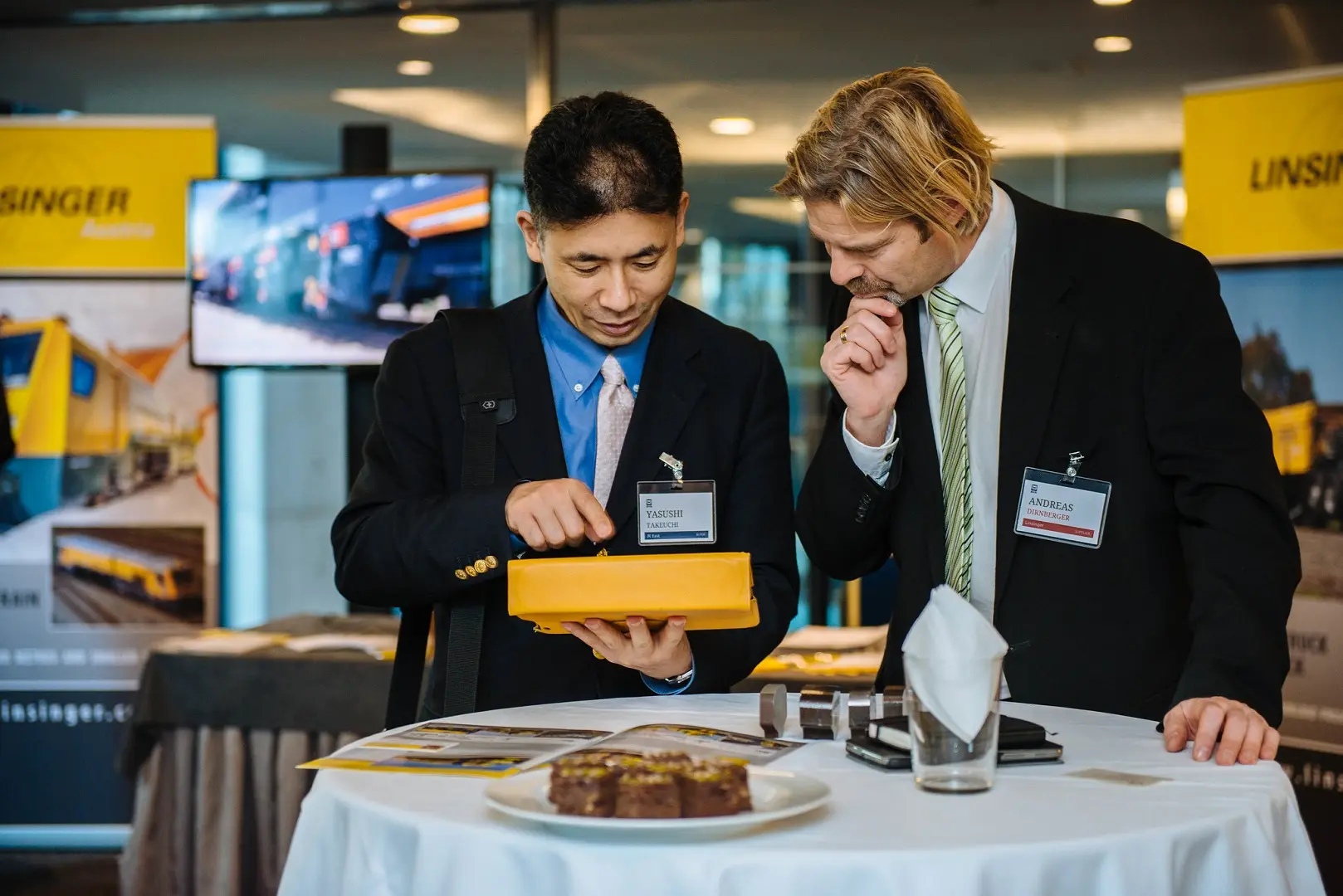Two professionals wearing suits and nametags examine a product at a trade show.