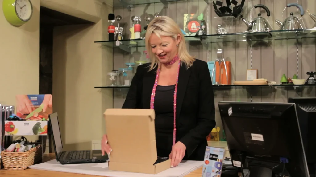 A salesperson opens a carboard box at her sales counter next to her laptop.