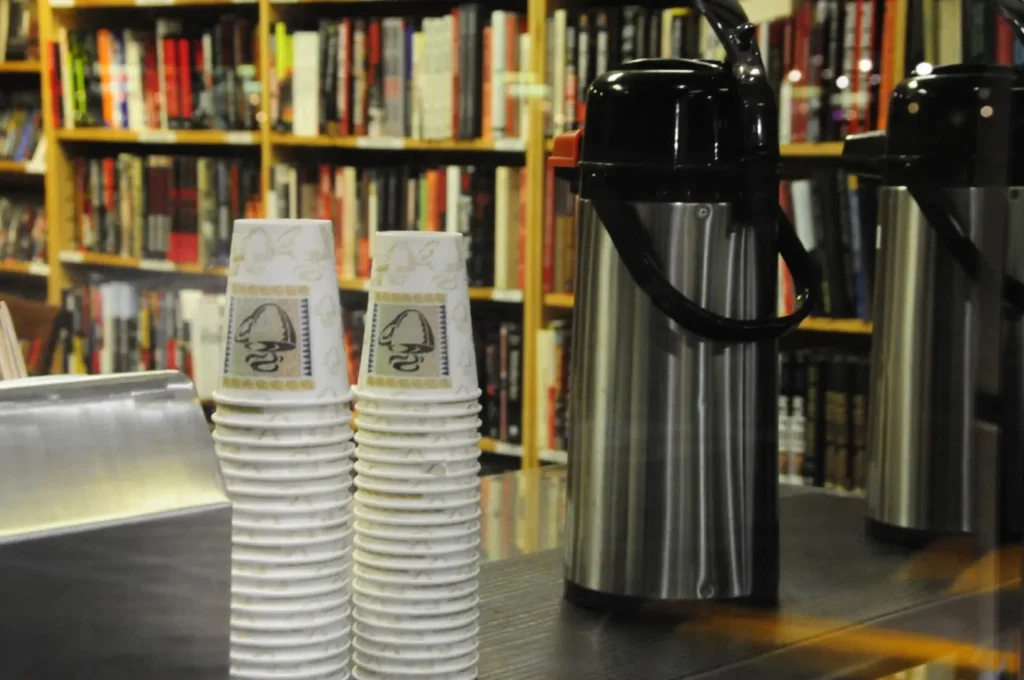 Two flasks and stack of white cups on a table. 