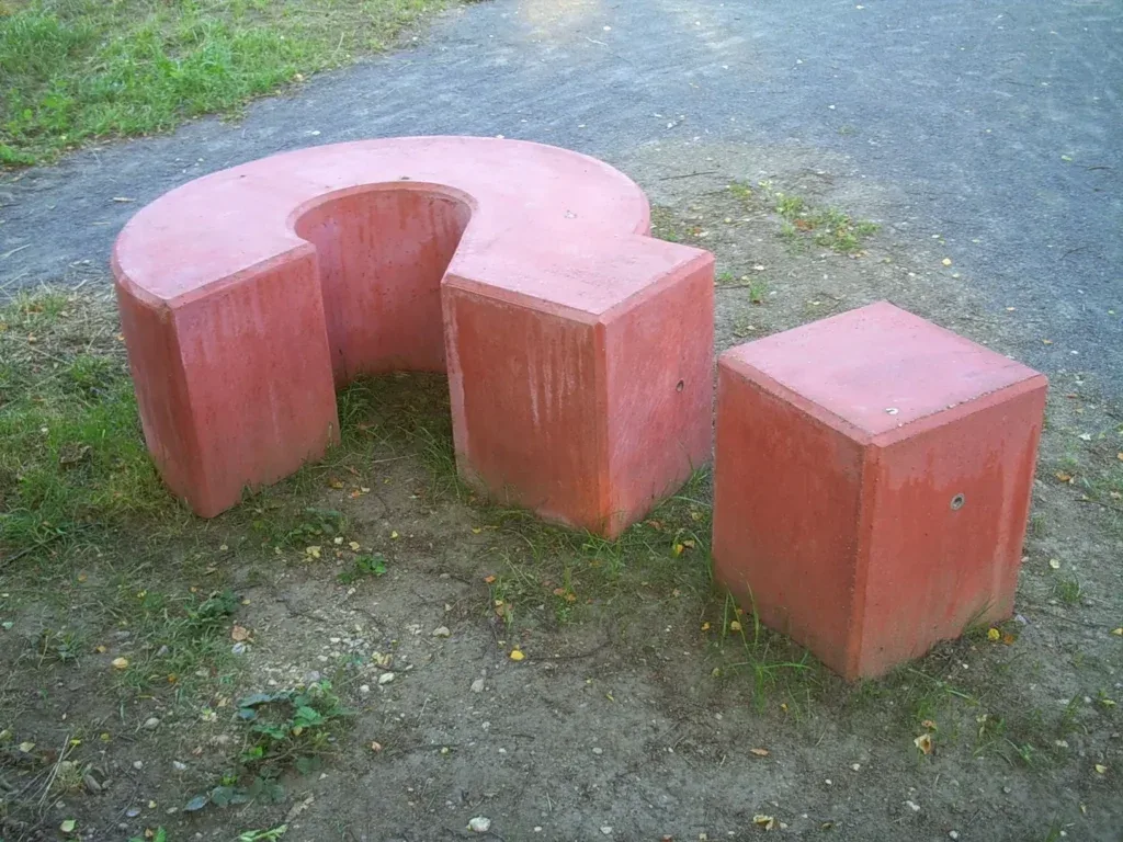 A red concrete bench in the shape of a question mark. 