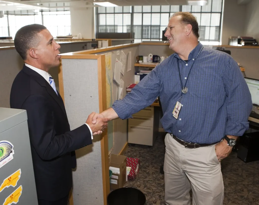 Two workers shake hands in an office cubicle. 