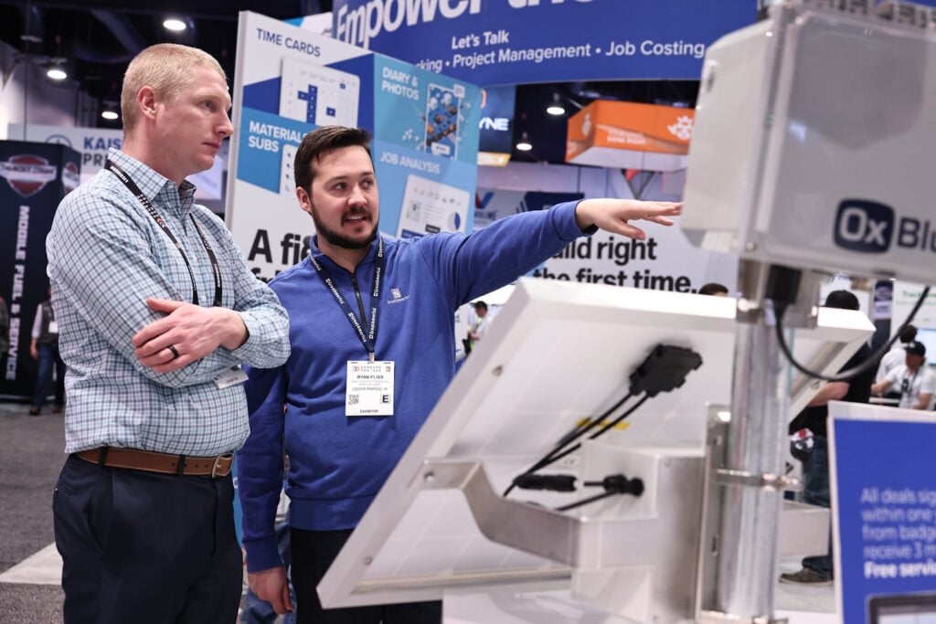 A company representative shows a trade show guest something on the trade show floor. 