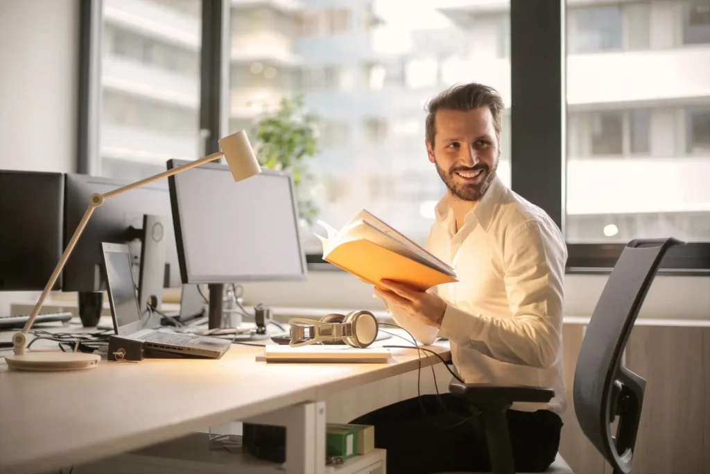 A man looks up from his book while sitting at his work desk.