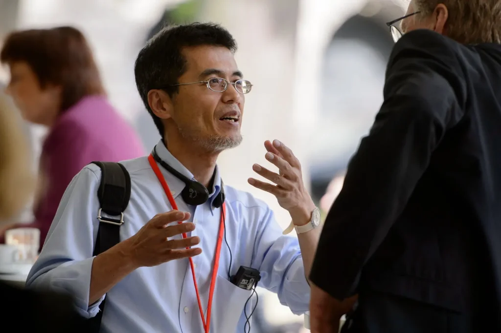 A man in glasses engaged in conversation with another professional.