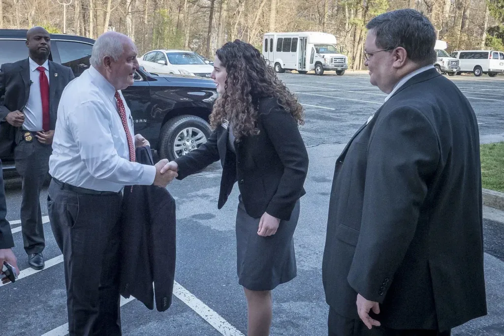 Two professionals greet one another in a car park.