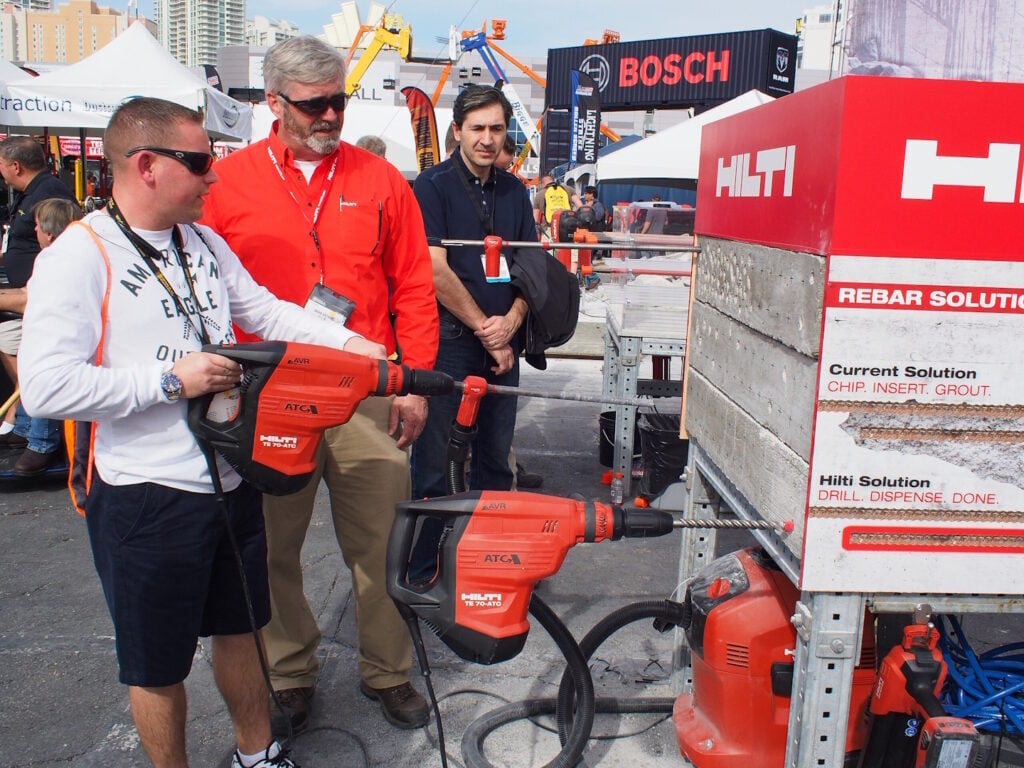 An employee watches on as a trade show visitor tests out a large drill.