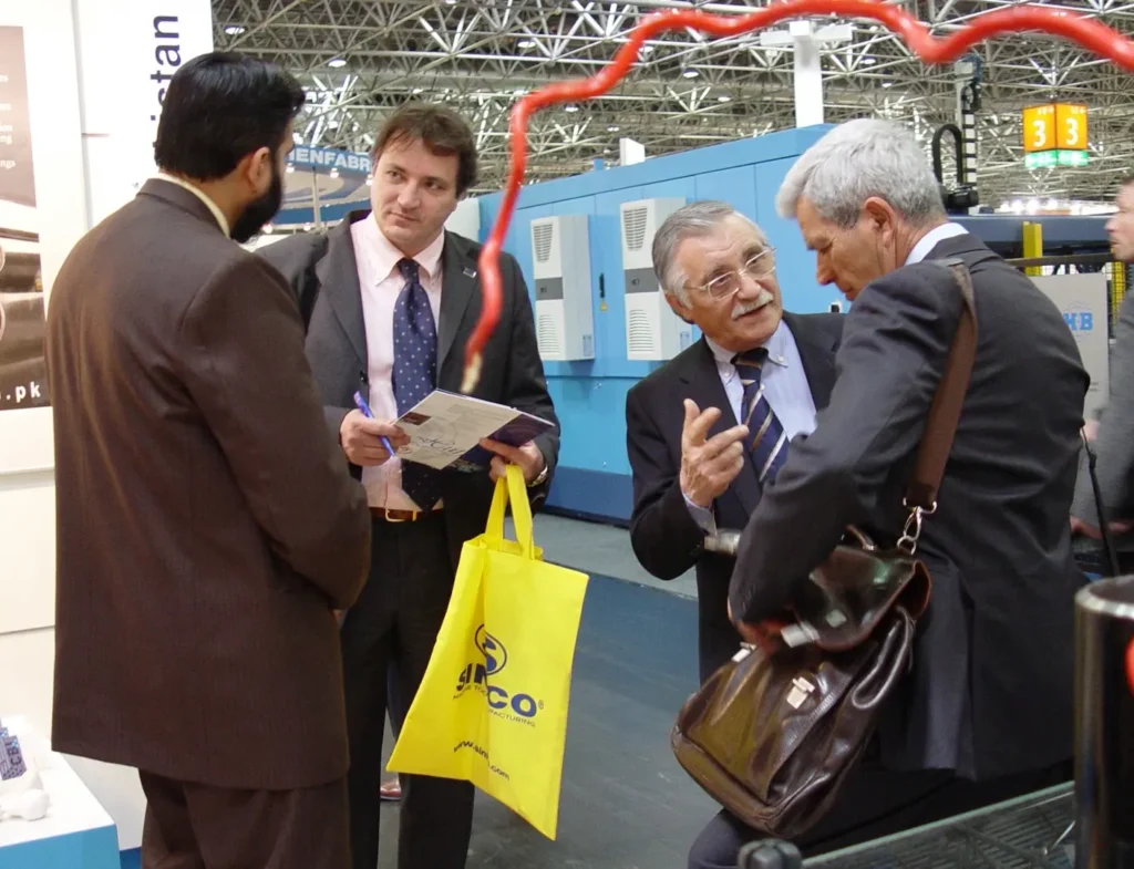 Four exhibition attendees converse amongst themselves at an exhibition booth.