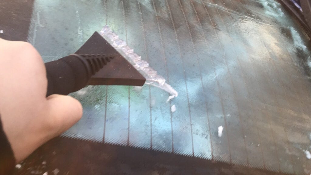 A person using an ice scraper to remove ice from a vehicle windscreen.