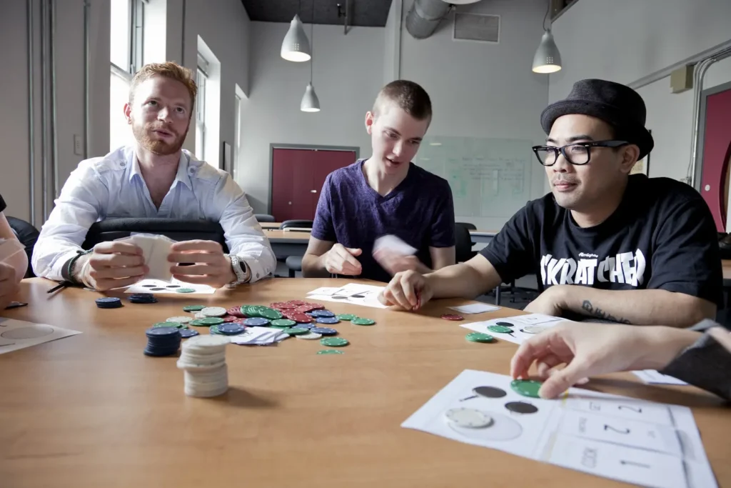 A group of people sitting around a table playing a game with poker chips.