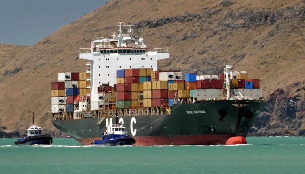 A large container ship being towed by two tugboats.