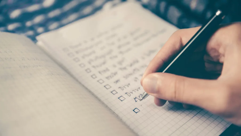 A hand writing a checklist in a notebook.